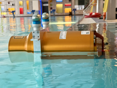 In einem Schwimmbad- bunter Hintergrund, blaues Wasser. IM Vordergrund ein oranger Zylinder